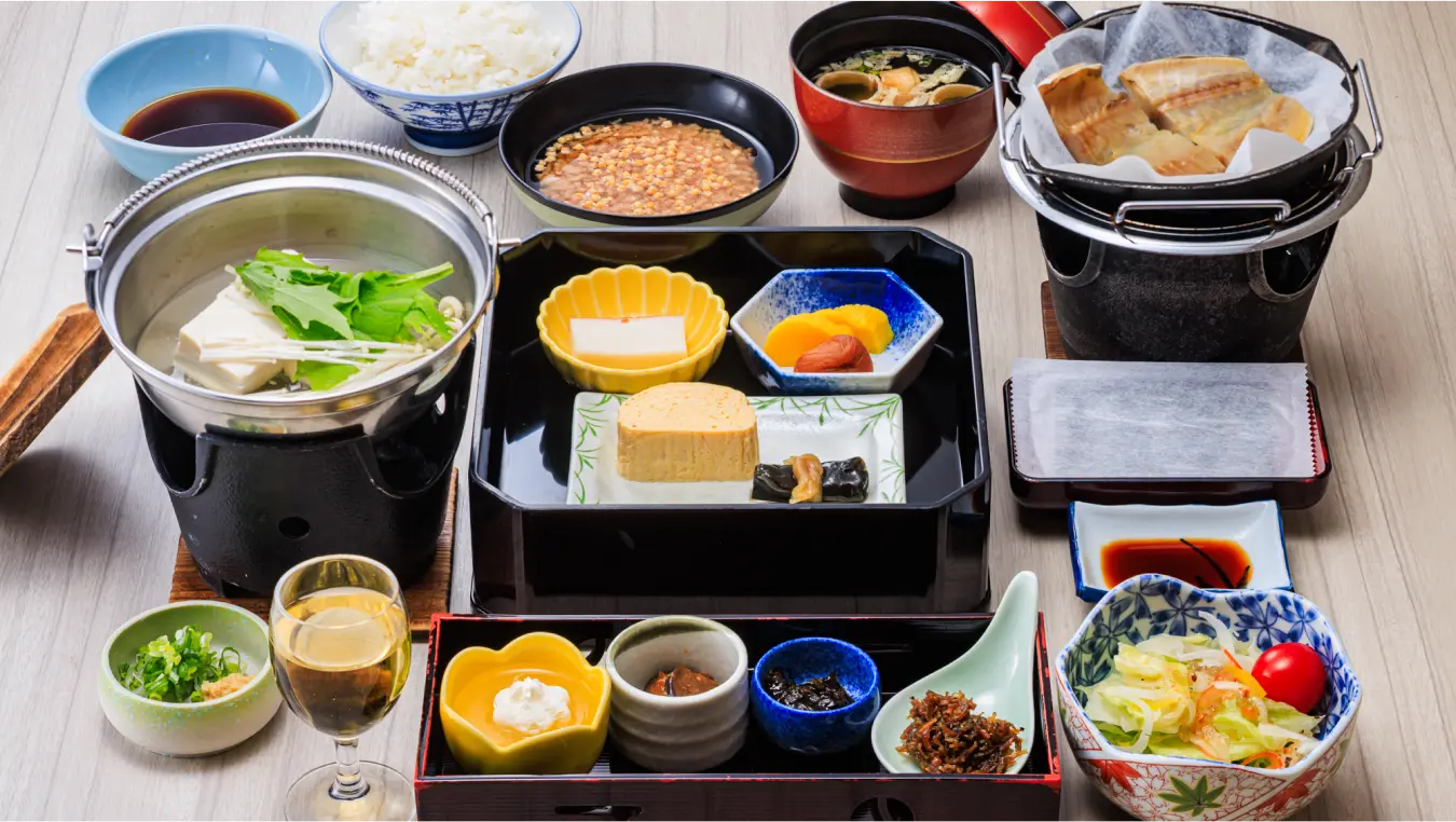 多くの小鉢が並んだ和朝食。豆腐鍋、ご飯、焼き魚など、様々な品が美しく盛り付けられている。