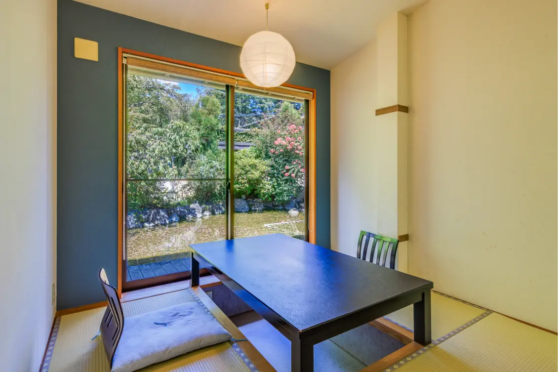 掘りごたつ式の個室ダイニング。窓の外には庭園が見え、テーブルと座椅子が置かれている。