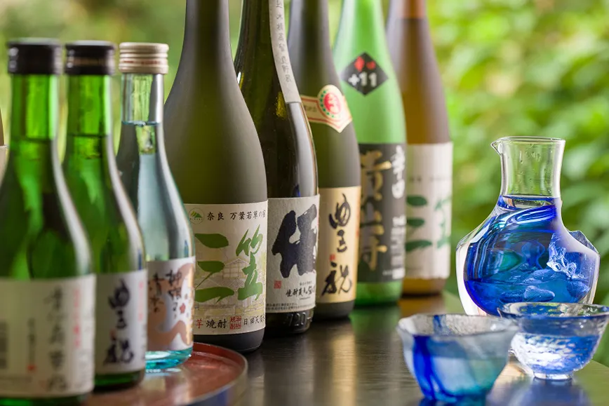 数種類の日本酒の瓶と青いガラスのお猪口