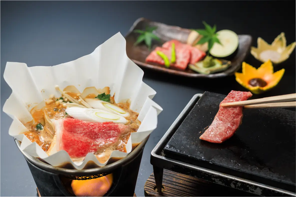 鍋料理と石板で焼く肉料理。箸で肉を掴む様子。