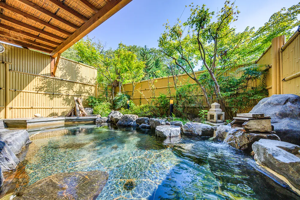 青空の下の露天風呂、岩に囲まれた開放的な湯船。