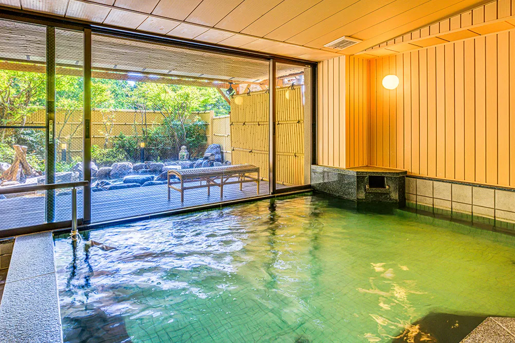 大きな窓から庭園が見える内風呂。広い湯舟の横にはベンチが置かれています。