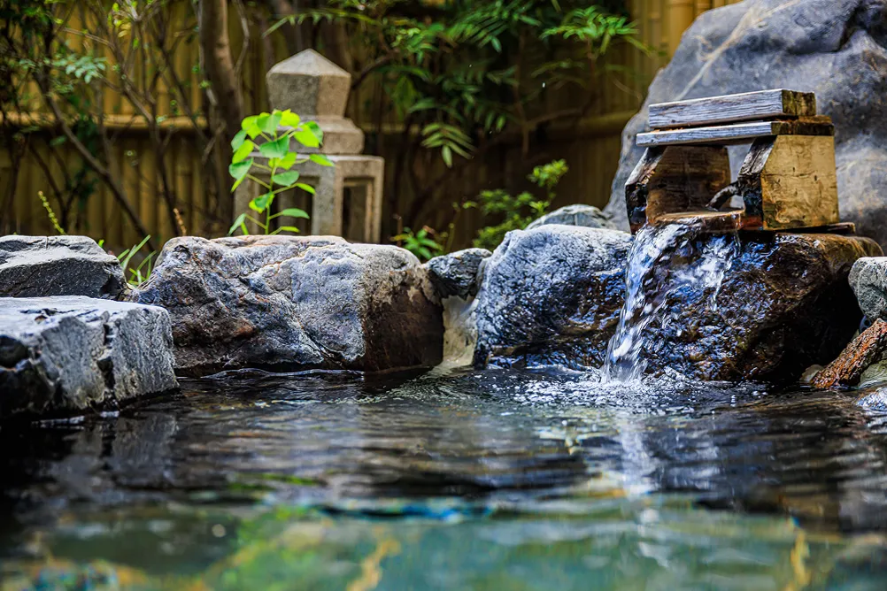 岩に囲まれた露天風呂。湯口からお湯が流れ落ちている様子。