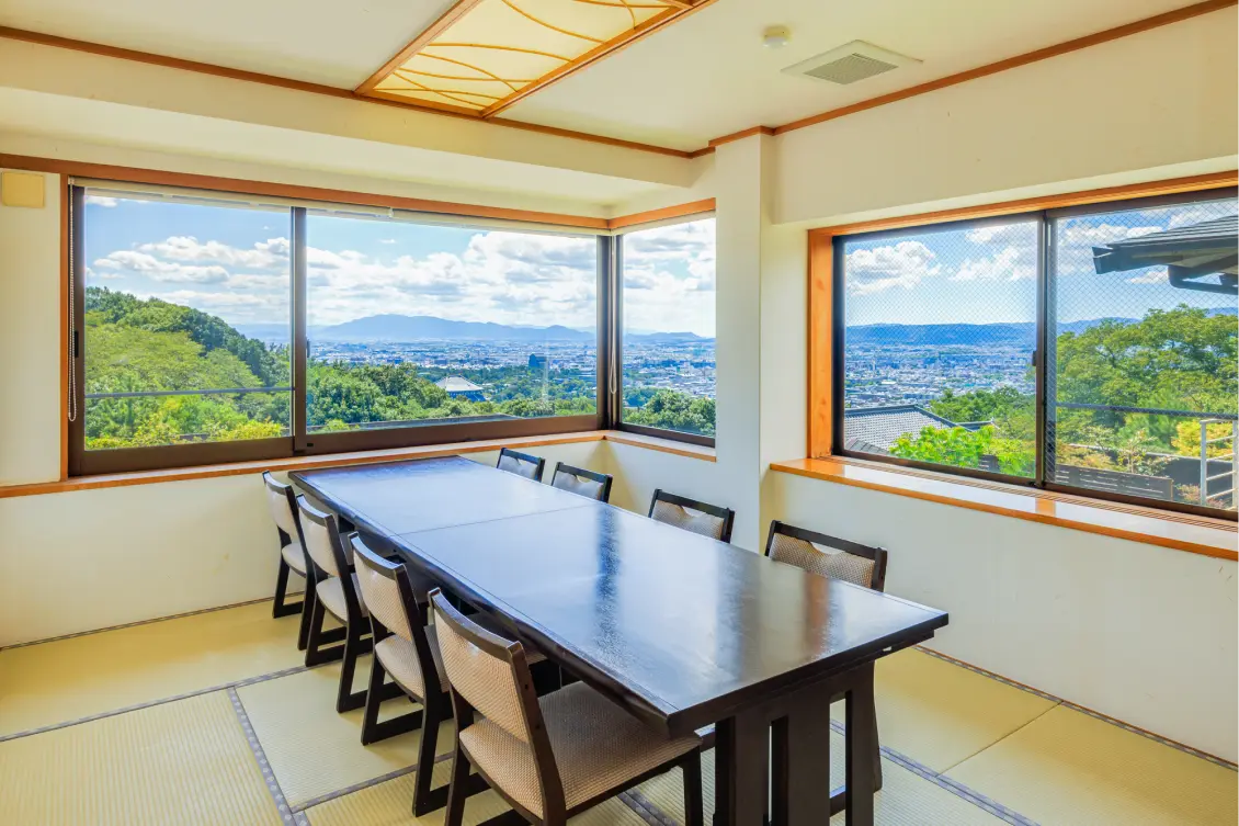 畳の個室ダイニング。長いテーブルと椅子が置かれ、窓からは広がる街並みが見える。