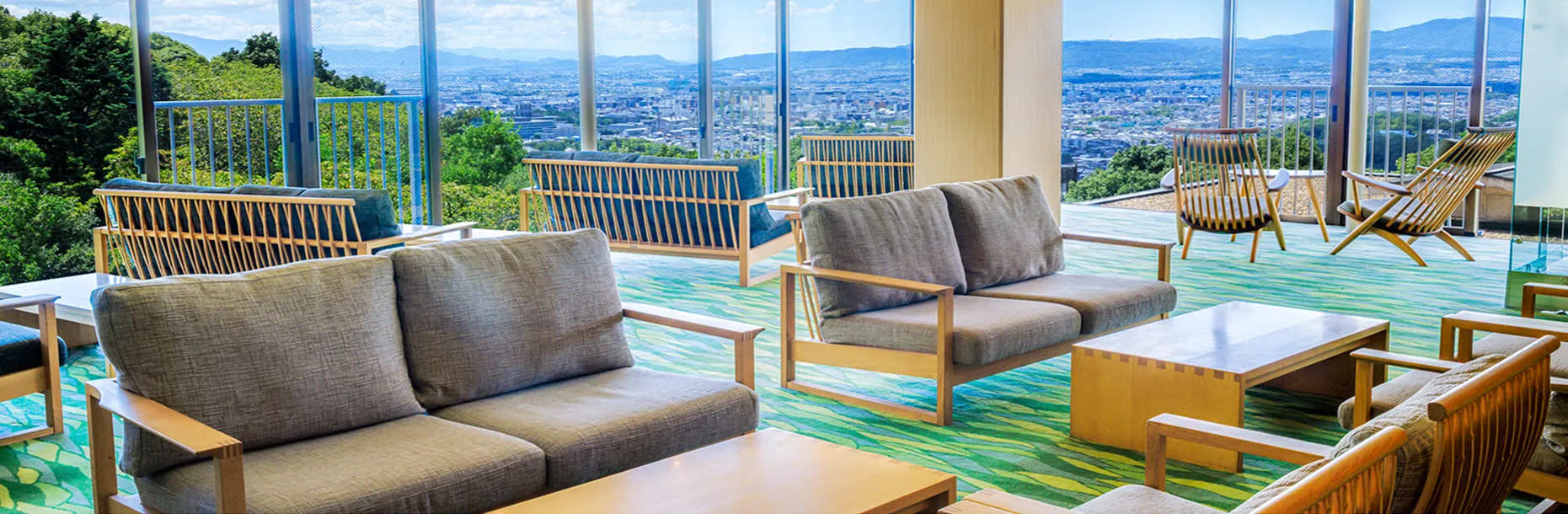 大きな窓から街並みを一望できるラウンジスペース、ソファとテーブルが並ぶ明るい空間