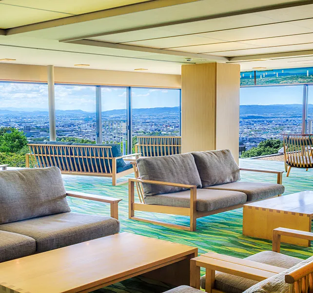 大きな窓から街並みを一望できるラウンジスペース、ソファとテーブルが並ぶ明るい空間