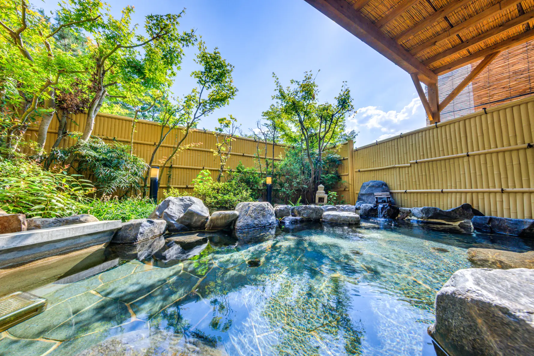 岩風呂の露天風呂。竹垣に囲まれ、湯舟の奥には庭園が見えます。