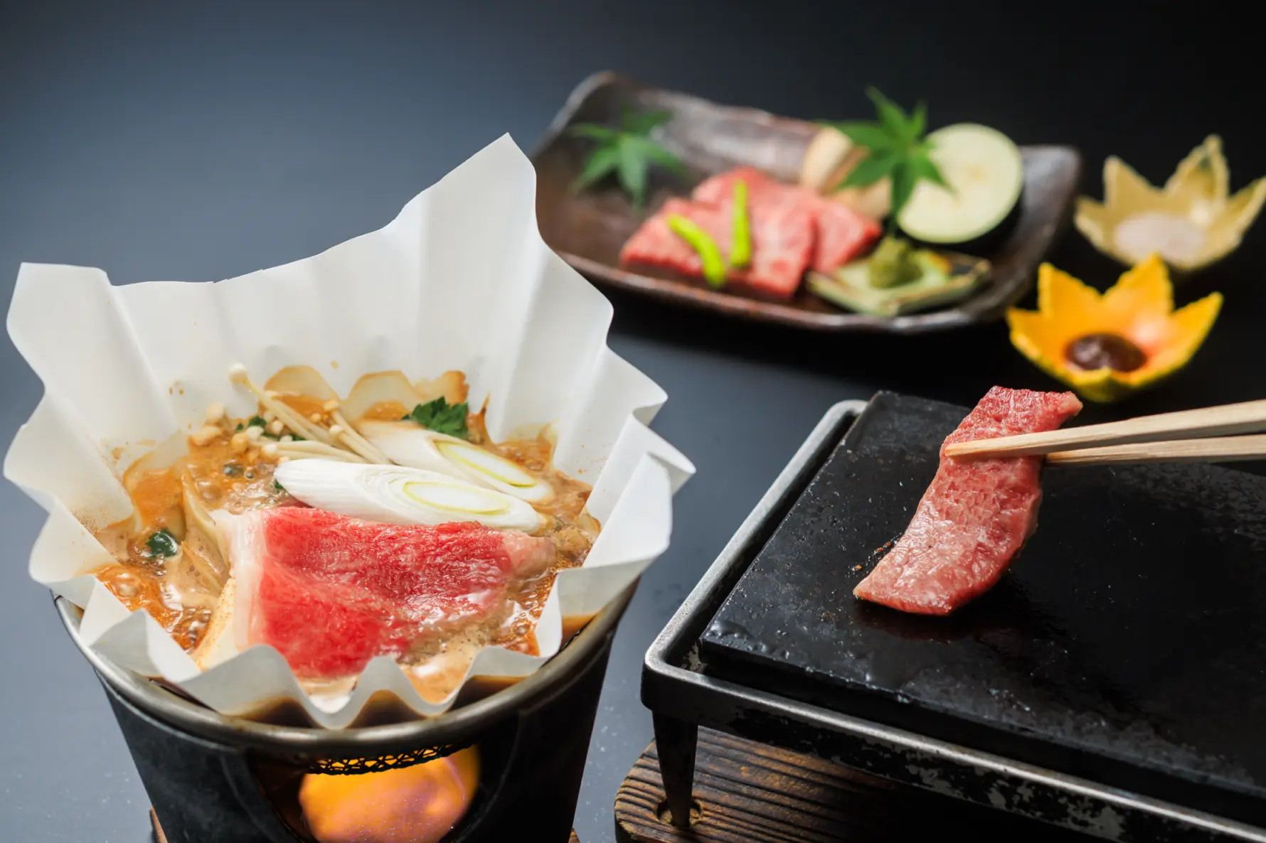 黒いテーブルに置かれた和食の料理。肉と野菜が入った鍋、石板で焼く肉料理などが並んでいます。