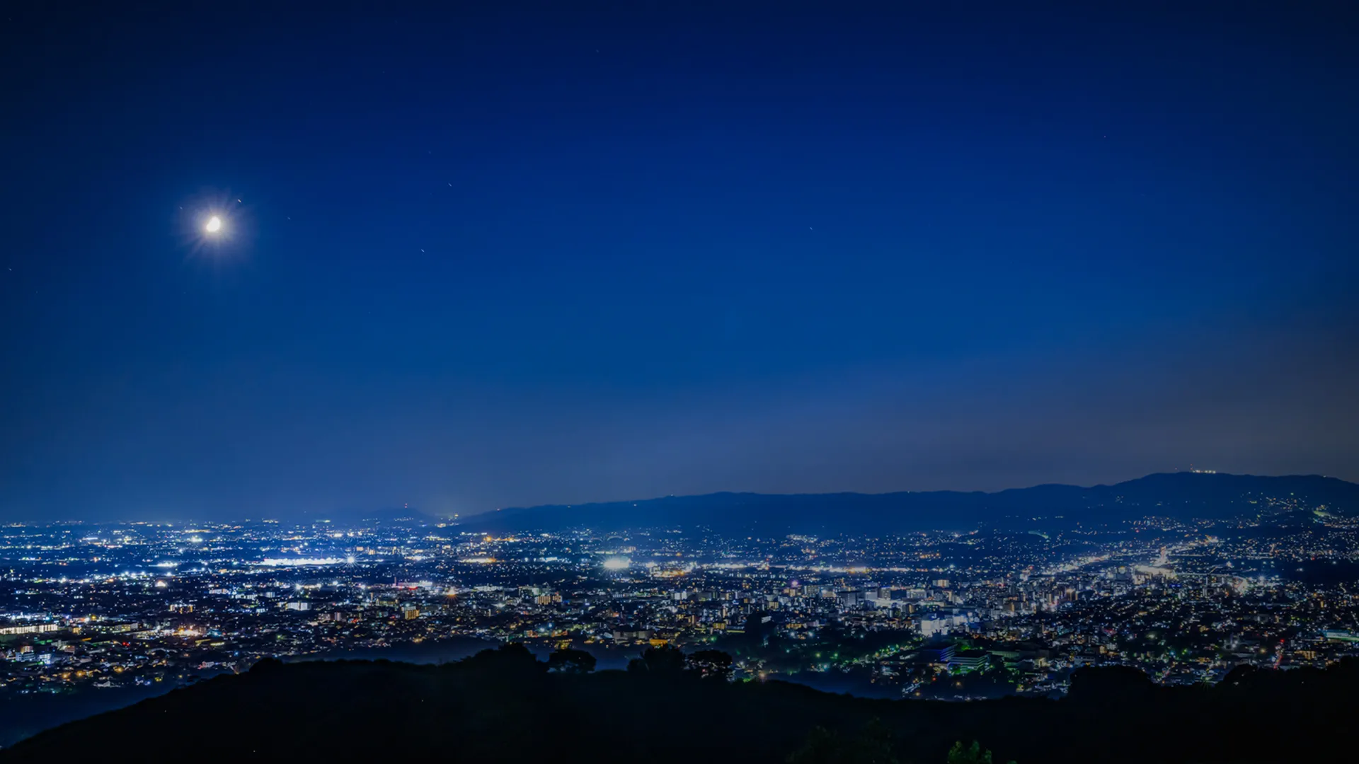 若草山から見下ろす奈良市街の夜景。濃紺の空の下、広大な街の明かりが遠くまで広がる。