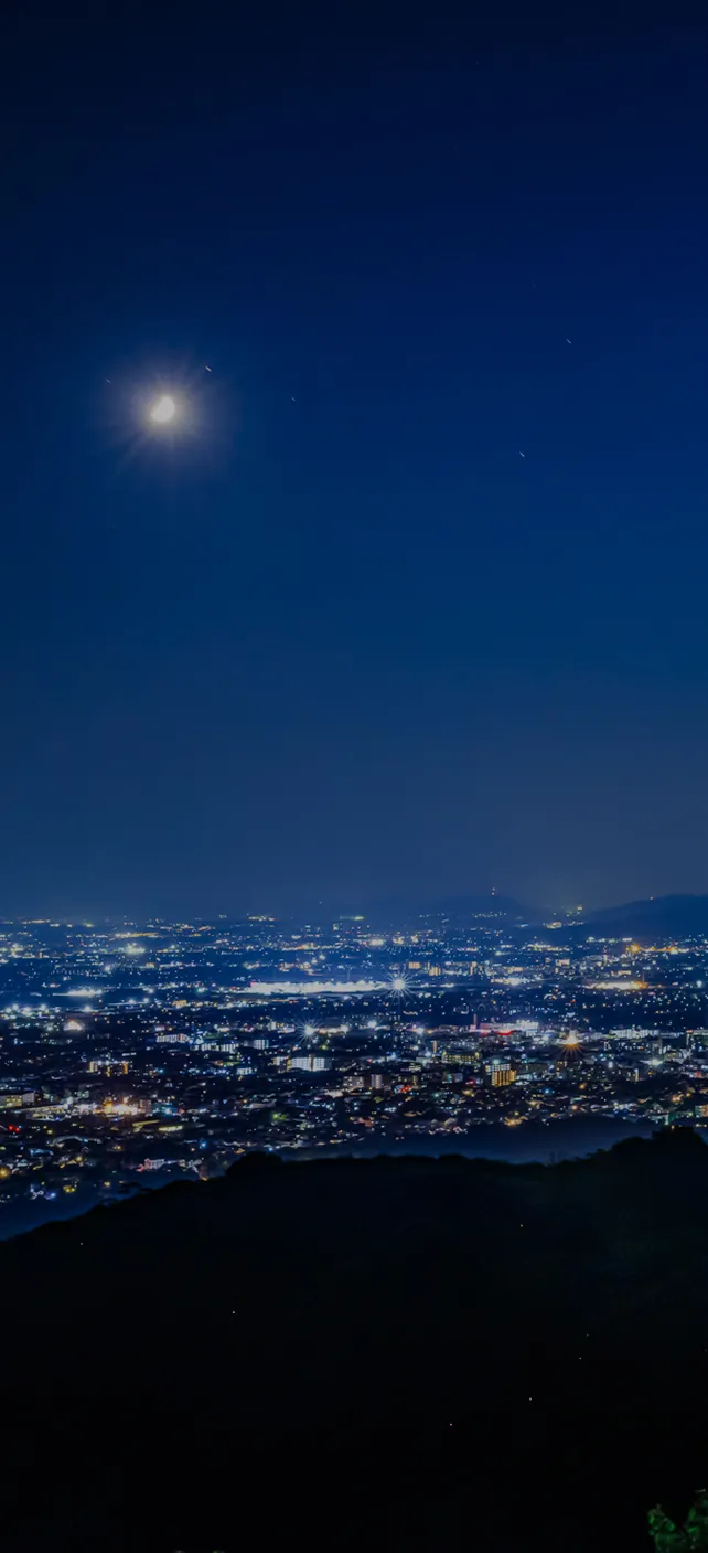 若草山から見下ろす奈良市街の夜景。濃紺の空の下、広大な街の明かりが遠くまで広がる。