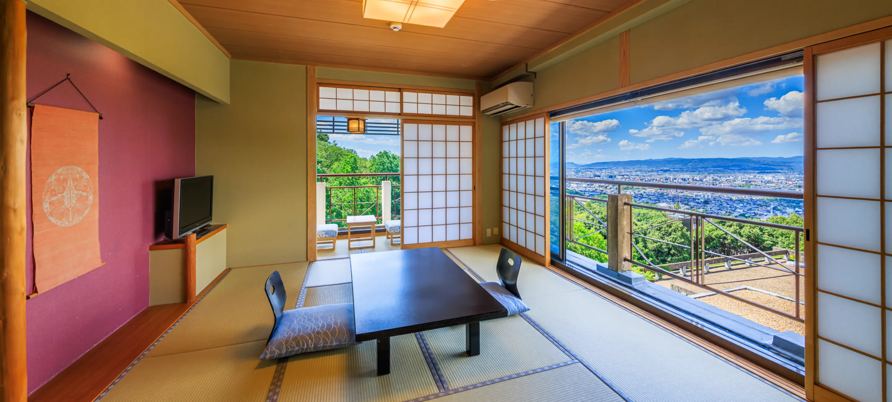 畳の部屋に置かれた黒いテーブルと座椅子。障子と大きな窓からは、青い空と広がる街並みが見えます。