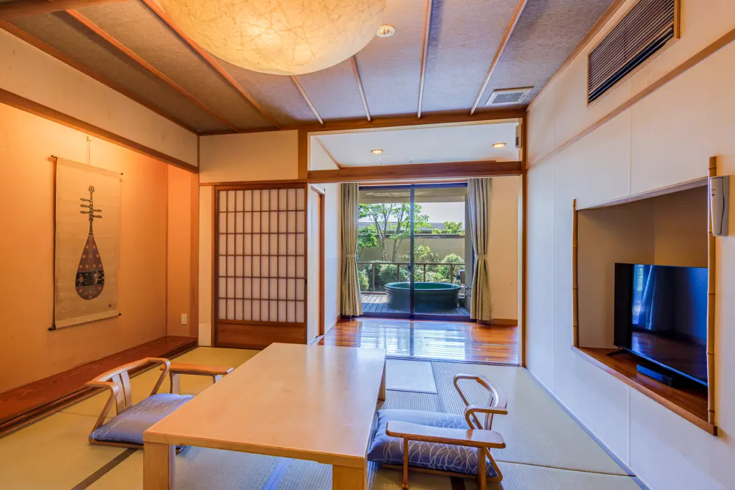テーブルと椅子が置かれた和室。奥には露天風呂付きのテラスが見える客室。