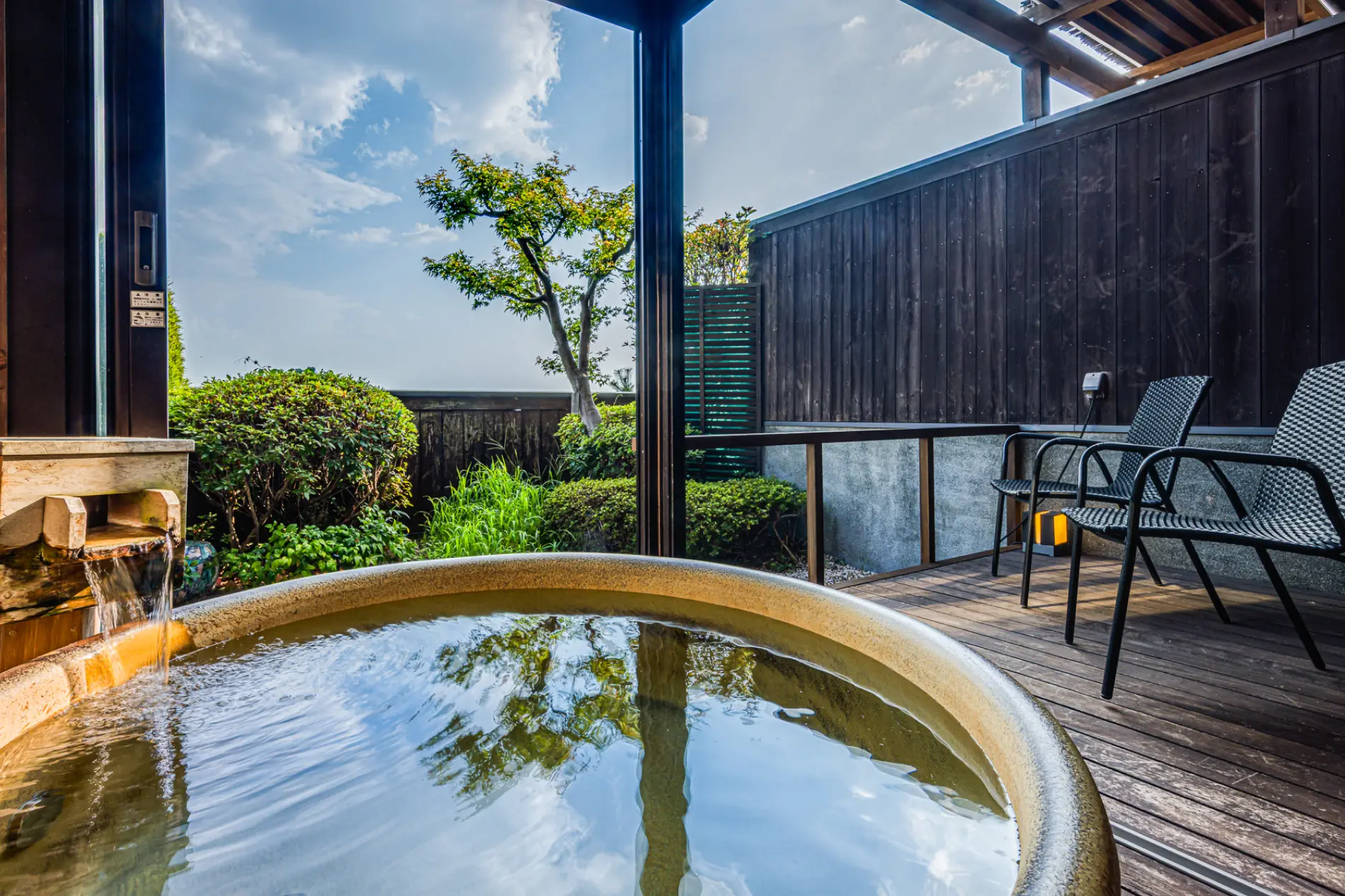 開放的な露天風呂。露天風呂の隣には椅子が置かれ、庭には木々が生い茂っています。