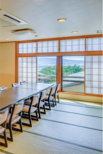 長いテーブルが置かれた和室の宴会場。窓からは街の景色が見えます。