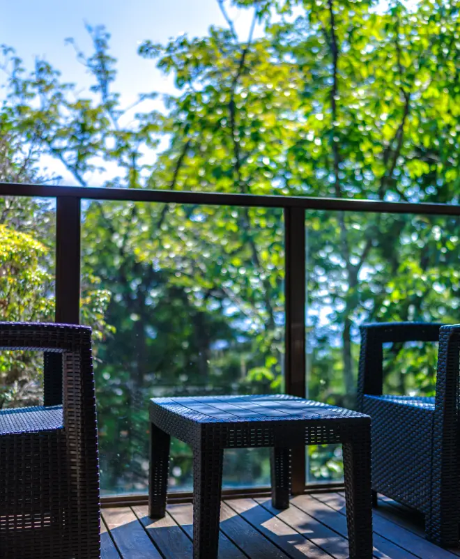 緑の木々が見える客室のテラスに置かれた、ラタン製のテーブルとチェア。