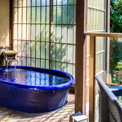 大きな窓の向こうに庭園と青い露天風呂が見える写真。