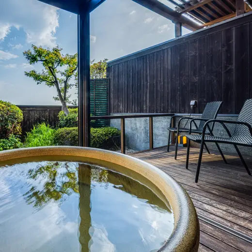 木のデッキテラスに置かれた丸い石造りの露天風呂と、その奥のチェア。