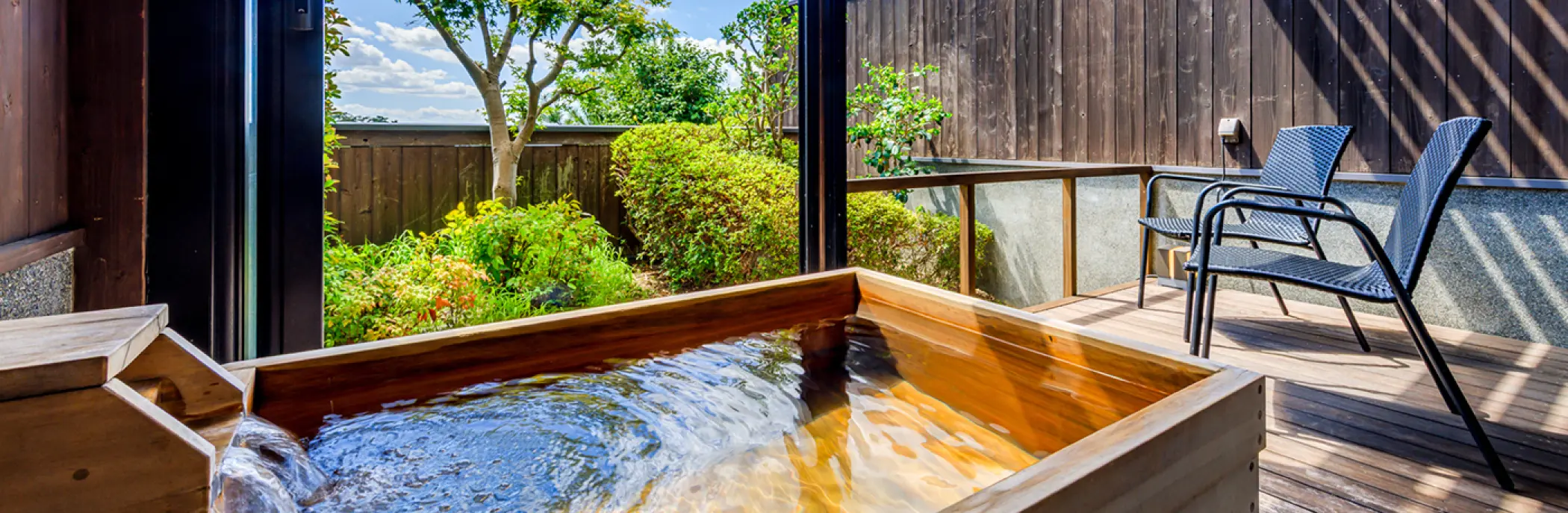 木製の露天風呂（温泉）と庭園が見えるデッキ
