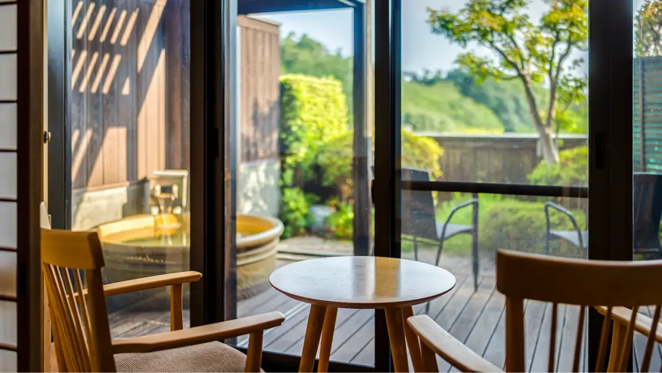 木製露天風呂（温泉）が見える窓際の椅子と円形テーブル。