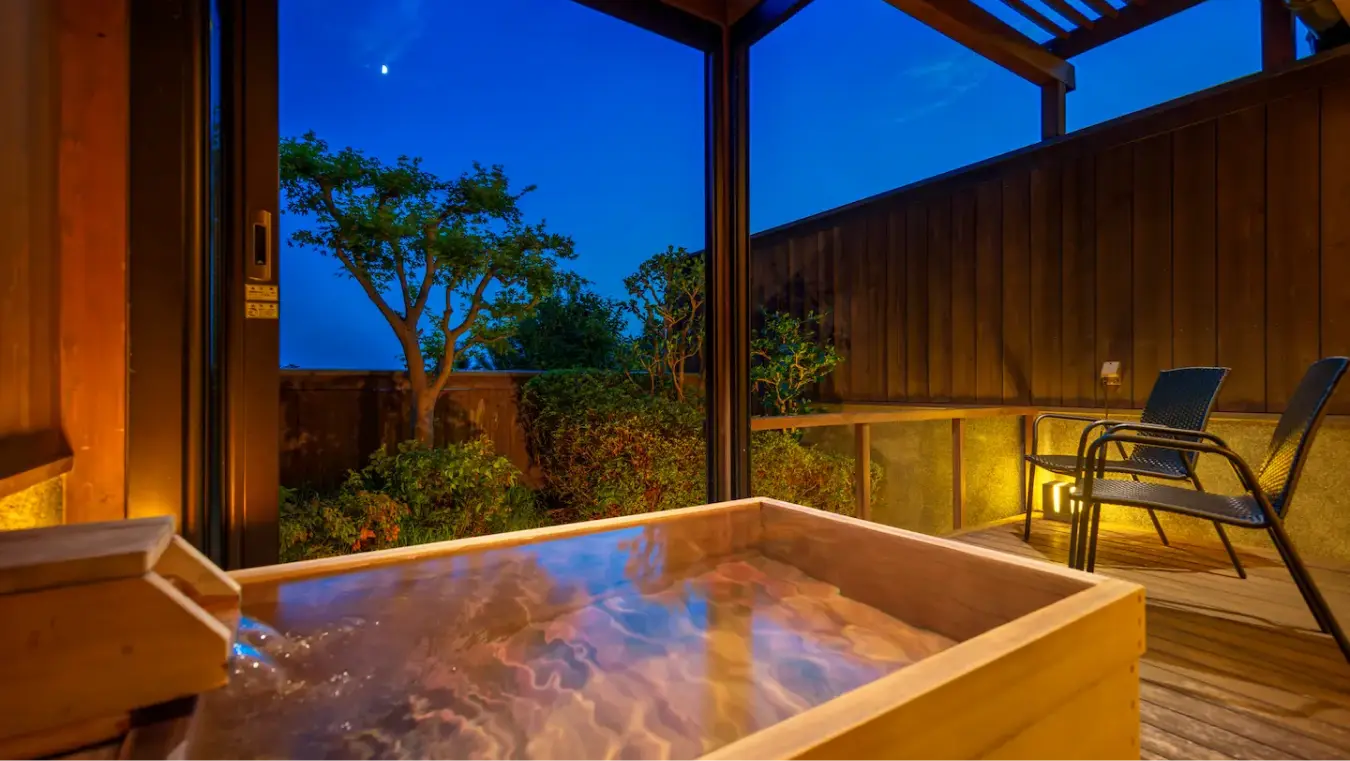 夜のデッキにある、湯気が立つ木製の露天風呂（温泉）。