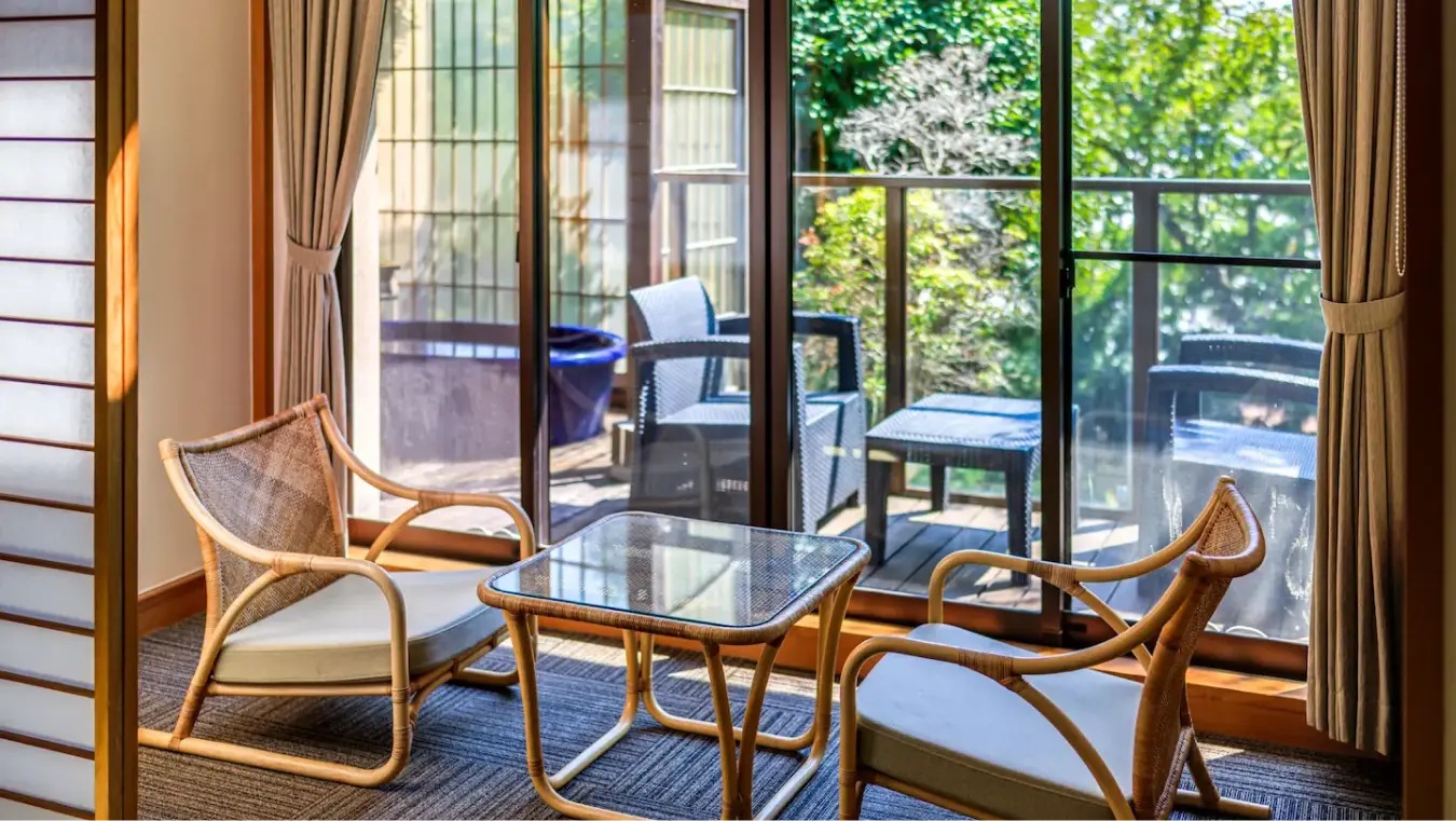 テラスの屋外家具と庭の緑が見える窓際の椅子とテーブル。