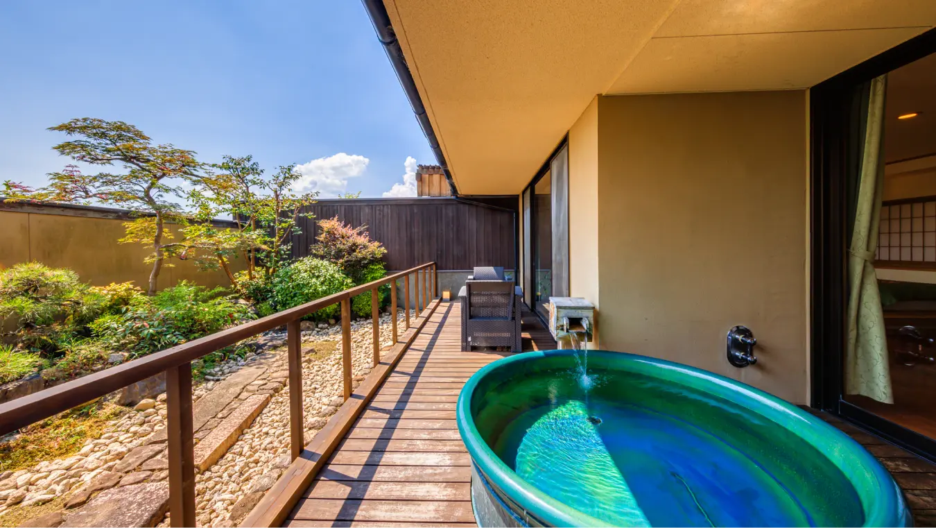 岩と植栽のある庭に面したデッキにある露天風呂。
