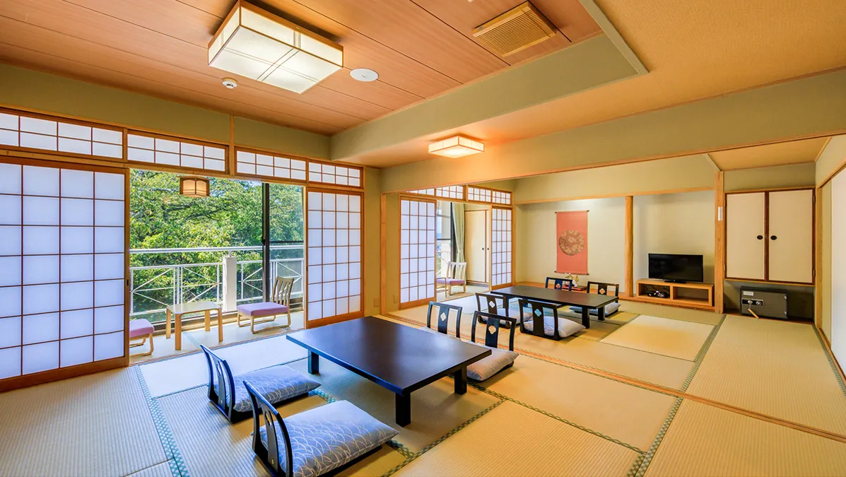 テーブル・座椅子が並んだ大部屋和室と、窓越しに見える自然の景色