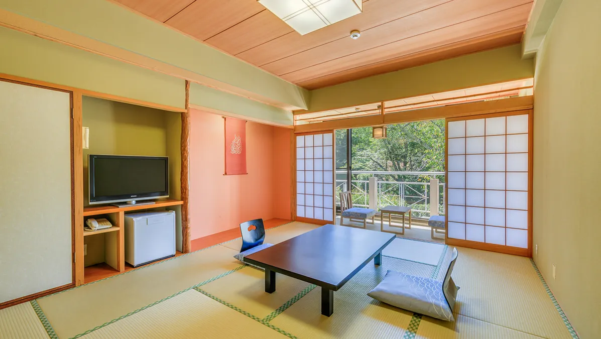 テレビ、テーブル、座椅子が設置された和室とバルコニーに広がる自然の眺め