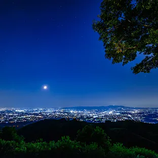 満月が輝く夜空と、夜景が広がる奈良の山中からの眺め。