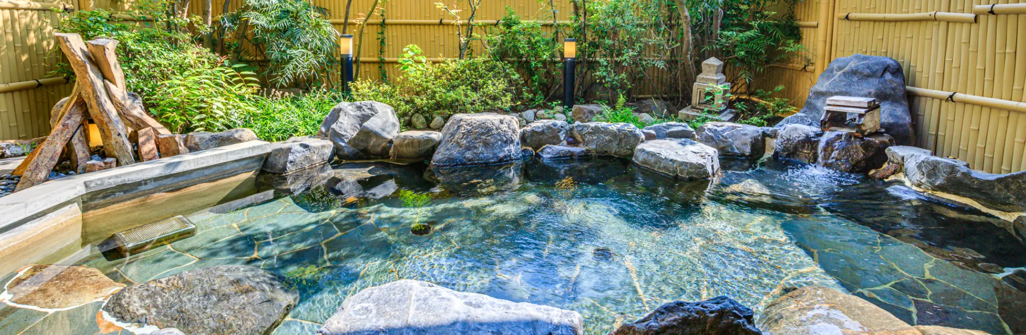 岩や緑に囲まれた露天風呂。空の光が水面に反射して輝いています。