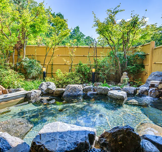 岩や緑に囲まれた露天風呂。空の光が水面に反射して輝いています。