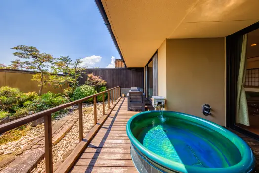 客室にある露天風呂。緑色の浴槽が置かれ、庭園が見えます。