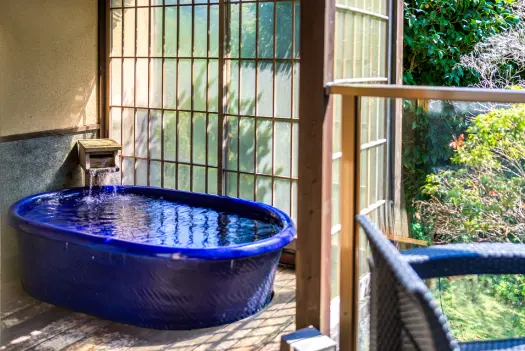 青い浴槽が置かれた客室の露天風呂。窓の外には緑が見えます。
