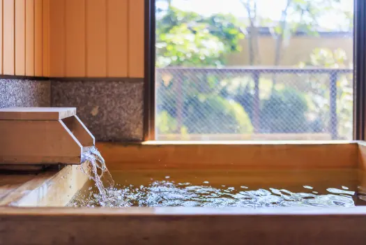木製の浴槽が置かれた客室の露天風呂。窓からは光が差し込んでいます。