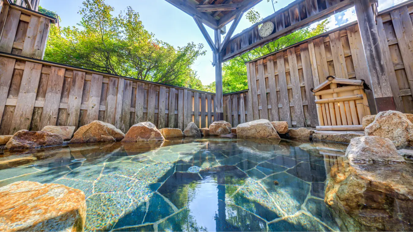 岩に囲まれた露天風呂。湯口からお湯が流れ落ち、青空が気持ちよさそうです。