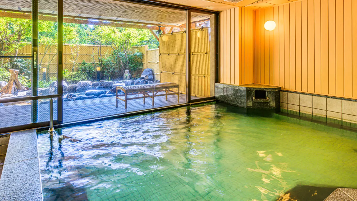大きな窓から庭園が見える内風呂。広い湯舟の横にはベンチが置かれています。