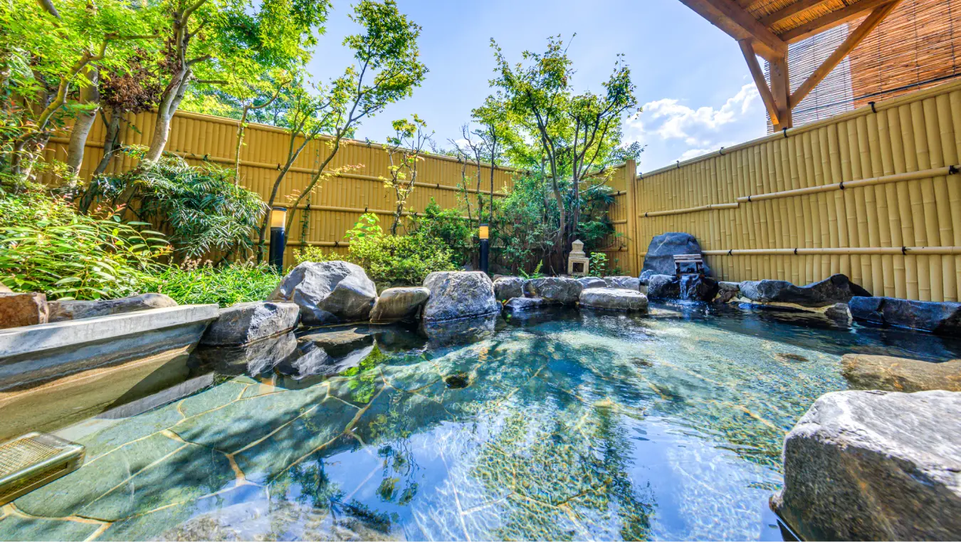 岩風呂の露天風呂。竹垣に囲まれ、湯舟の奥には木々が生い茂っています。