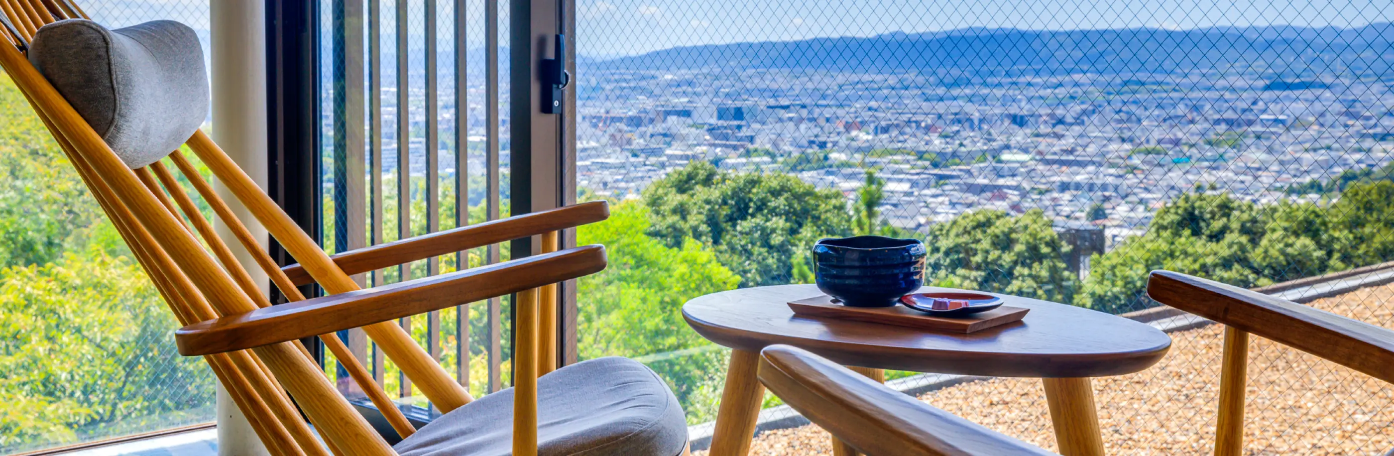 奈良県の街並みが一望できる窓際の席で、抹茶と和菓子が置かれたテーブルと、2脚の木製チェア。