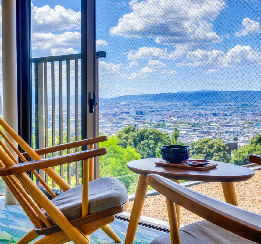 奈良県の街並みが一望できる窓際の席で、抹茶と和菓子が置かれたテーブルと、2脚の木製チェア。