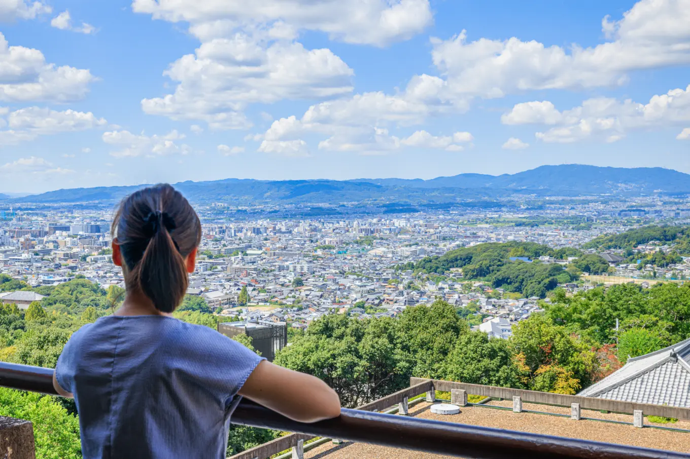 女性が後ろ向きで、奈良の街並みを一望できる展望台から景色を眺めている写真。