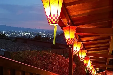 ライトアップされた提灯が並ぶ回廊から、奈良市街地の夜景を一望する光景。